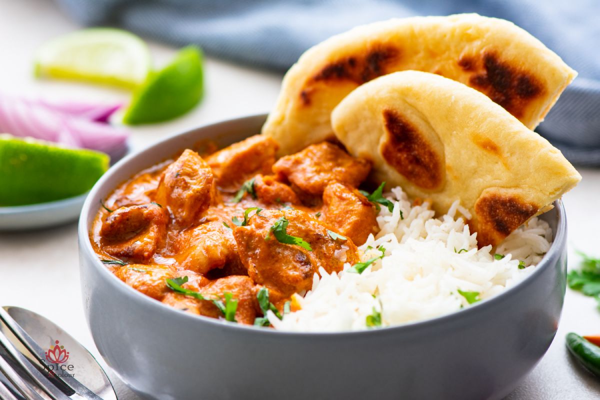Butter Chicken servido con arroz basmati y naan, cubierto con salsa cremosa y hojas de cilantro por encima.